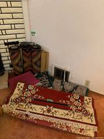 Small area rugs and runners shown stacked and rolled against a wall near a vent and brick feature, various colors and designs visible.