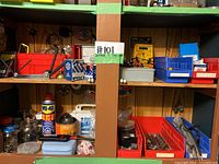 Two wooden shelves holding assorted small tools, parts, a precision screwdriver set, WD-40, first aid kit, and multiple bins with screws and hardware.
