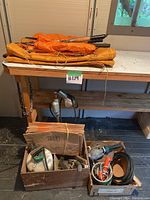 Photo of orange tarps stacked on a wooden bench with boxes of assorted tools and equipment underneath