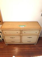 Front view of vintage beige dresser with six drawers and metal handles showing wear.