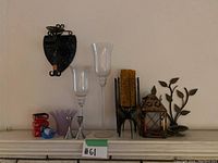 Wide view of candleholders and decor arranged on a mantle displaying wall sconce, glass and metal candleholders, lantern and decorative branch.