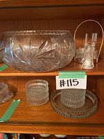 Wide view of the large hand-cut crystal bowl, smaller pressed glass bowls and plates, and cruet set with metal handle in wooden cabinet shelf