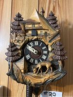 Front view of the vintage German cuckoo clock showing the carved wooden chalet, trees, and deer around the clock face with Roman numerals.