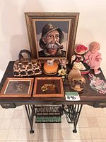 Full view of all vintage needlepoint and decor items on wooden table including framed artworks, figurines, dolls, and purse