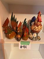 Group shelf photo showing three wooden rooster figurines, a small copper pitcher, and a large ceramic rooster with floral details.
