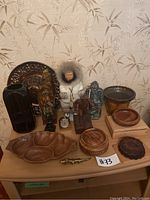 Photo showing the full lot of vintage sculptures and figurines including carved wood statues, a doll in parka, decorative plates, and various wooden and ceramic containers.
