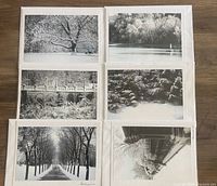Six black and white photography greeting cards laid out in two rows of three on a wood surface. Scenes are winter landscapes featuring trees, a bridge, river, and snow.
