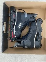 Side view of the pair of Bauer men's rollerblades inside a cardboard box showing the frame, wheels, and boot details.