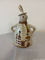 Front view of the ceramic snowman tea light candle holder showing facial features, hat, scarf, and village cutouts