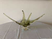 Chalet art glass centerpiece bowl with flowing extended arms, displayed on a white textured tablecloth, photographed against plain wall.