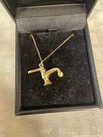 Gold plated necklace with faucet-shaped pendant displayed in black jewelry box.