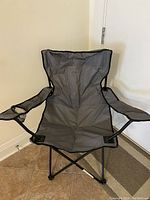 Front view of foldable camping chair showing gray fabric and black metal frame, armrests with cup holder on one side.