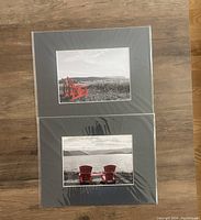 Two matte mounted black and white photography prints with red Adirondack chairs in Newfoundland scenes, laid flat on wooden floor.