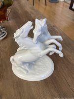 Front angled view of white porcelain fighting stallions figurine showing dynamic pose and details.