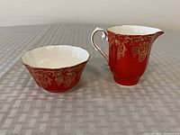 Photo of the creamer jug and open sugar bowl, showing red porcelain with gold grapevine pattern, in good condition.