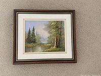 Front view of the framed signed oil painting showing trees by a water body and forest background.