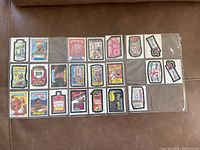 22 different Wacky Packages parody stickers from the 1980s inside a clear plastic protective sleeve, laid out on a brown surface.