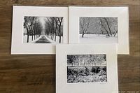 Photo of three black and white winter photography prints, each 5x7 inches, matted to 8x10 inches, showing snowy outdoor scenes with trees, a bench, and a fence.