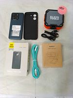 All items laid out: Blackview smartphone, phone case, Klein Tools Bluetooth speaker with cable, Aukey webcam sealed box, portable power bank, turquoise USB cable