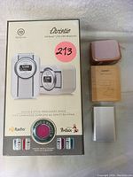 Photo showing the Christie HD Radio box with retro design in white/silver color, the Aukey portable speaker in rose gold, and the Aukey 1080p webcam box in silver.