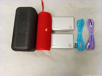 Overall lot contents with JBL Flip 5 speaker, black protective case, two white power banks, and two charging cables in blue and purple.