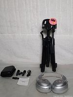 Black adjustable tripod stand with legs folded, silver Monster MH31902 headphones, wireless microphone receiver with two lapel microphones, carrying case, and instruction manual.