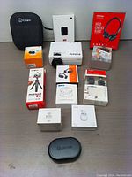 Overview of multimedia bundle with all boxed items including headphones, earphones, tripods, microphone, projector, security camera and accessories displayed on table