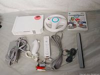 All items included in the Nintendo Wii bundle laid out, showing console, remote, nunchuk, Wii wheel, sensor bar, adapter, and Mario Kart game disc case.
