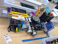 Overview of art supplies lot showing pencils, acrylic paints, brushes, markers, scissors, tape and glue tool.