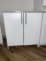 Front view of white 2-door cabinet with metal handles showing wear on floor-level base and minor scuffs.