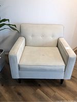 Front view of light beige upholstered armchair showing button tufted backrest and seat cushion with visible stains.