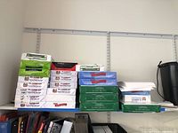Stack of 24 packs of copy paper on a shelf including Flagship Bright and Hammermill packages.