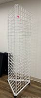 Full view of the white three-sided metal wire display tower standing upright on a wood floor.