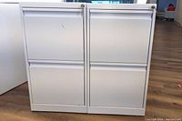 Front view of two white metal filing cabinets side by side, showing two drawers each with locks on top corners.