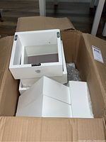 Seven white square floating wall display boxes stacked inside a cardboard box.