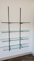 Front view of the entire glass shelving unit showing 4 glass shelves mounted on two vertical metal rails with brackets and braces.