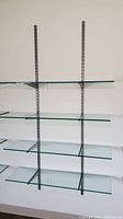 Four tempered glass shelves mounted on vertical metal rails, showing full view of shelves attached to wall.
