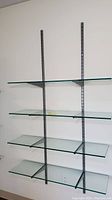 Front view of the 4 clear tempered glass shelves mounted on vertical metal rails with metal brackets.