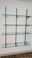 Front view of the glass shelving unit mounted on the wall showing four glass shelves with metal bracket supports.