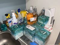 Full view of the lot on a counter with various hand sanitizers, surface cleaners, Blue Kleenex tissue boxes, and yellow Goo Gone container.