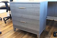 Front view of 2-drawer lateral file cabinet showing gray woodgrain laminate finish, silver handles and tapered legs