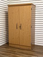 Full view of the closed pressing wood cabinet showing wood grain surface, two doors, black handles, and lock.
