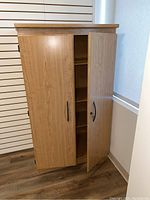 Front view of the wood grain locking cabinet with one door partially open showing the door handle and lock with key inserted.