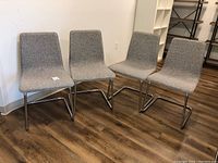 Photo showing four cantilever chairs with gray fabric upholstery and metal bases arranged on wood floor.