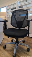 Front view of black mesh office chair with visible armrest wear.