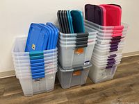 Three stacks of clear plastic bins with various colored lids (blue, turquoise, purple, pink, black) against a white wall