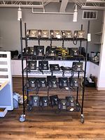 Front view of the black metal shelving unit loaded with office phones, showing five wire shelves on caster wheels in an office setting.