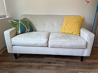 Front view of cream loveseat sofa with two pillows, one green-blue patterned and one yellow textured.
