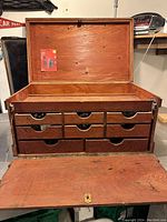 Open view of the toolbox showing plywood interior, hinged top lid, support chains, and seven drawers with semi-circular handles.