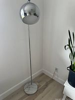 Full view of the chrome arch lamp showing the marble base, chrome stem, and dome shade near a wall corner.